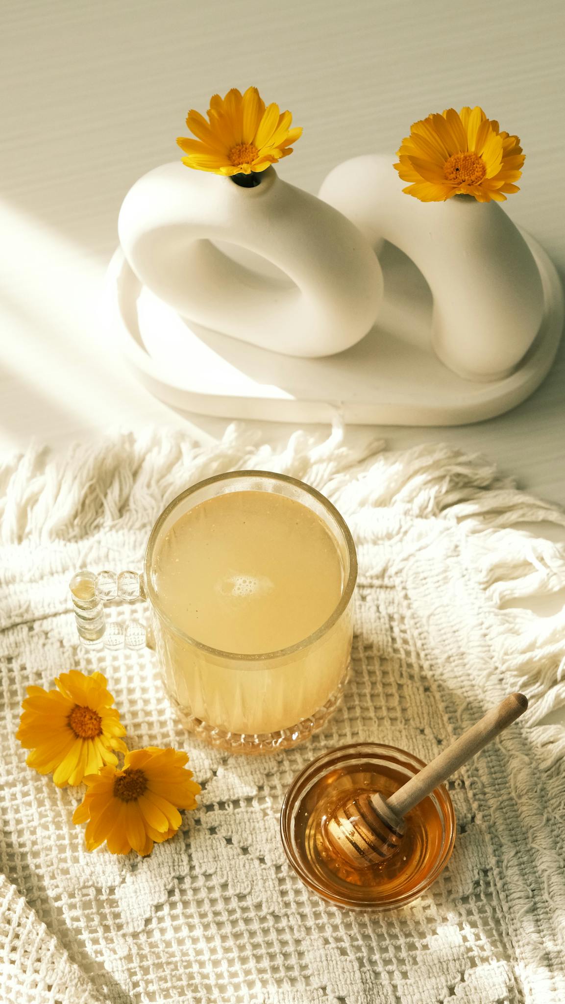 Aesthetic composition featuring honey, chamomile flowers, and a modern vase on a textured surface.